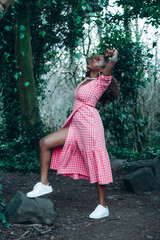 Beautiful African black woman in park. Beautiful young woman with brown skin. Smiling black woman with afro hair wearing pink gingham dress and pearls.