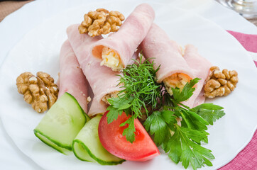 Ham rolls with cheese and nuts, with vegetables on a white plate close-up