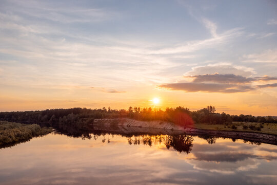 Colorful sunset over the river in the countryside. Drone photo of burning sun reaching the horizon with a huge calm river on the foreground