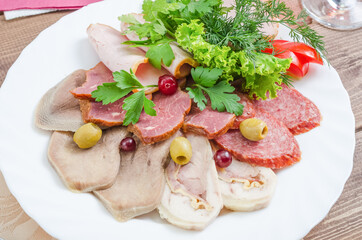 Cold cuts - tongue, smoked sausage, ham garnished with herbs on a white plate