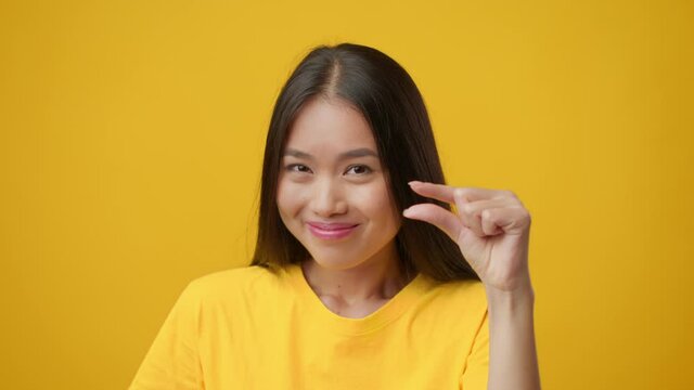 Japanese Lady Showing Tiny Size Gesturing With Fingers, Yellow Background