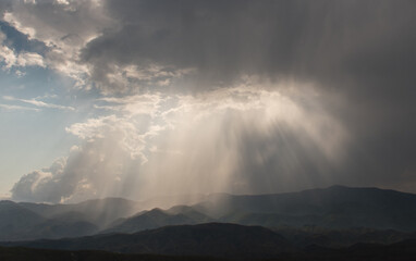 Fototapeta na wymiar Sunbeams breaking through clouds onto mountains below - horizontal