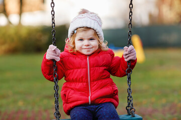 Cute toddler girl having fun on playground. Happy healthy little child climbing, swinging and...