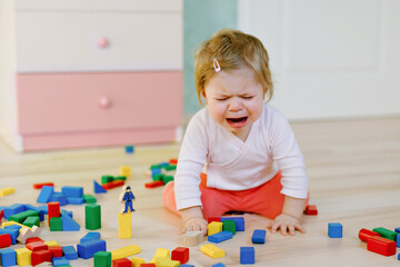 Upset crying baby girl with educational toys. Sad tired or hungry alone healthy child sitting near...