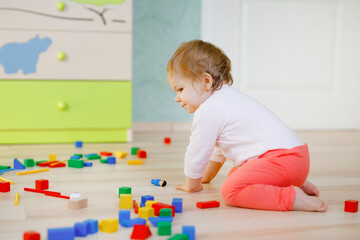 Cute baby girl playing with educational toys. Happy healthy child having fun with colorful different wooden blocks at home or nursery. Baby crawling, view from back, without face, unrecognizable