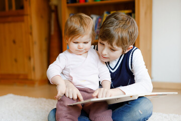 School kid boy reading book for little toddler baby girl, Two siblings sitting together and read...
