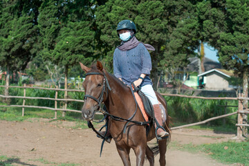 Women with mask and hijab learns to ride a horse. girls riding horses at the ranch. equestrian sport during the pandemic