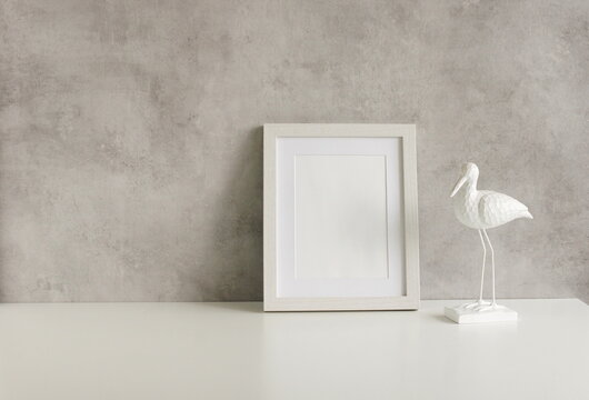 Frame mockup template and bird figurine on white table near gray wall . Copy space. Minimal concept. Interior wall accessories photo frame, poster.