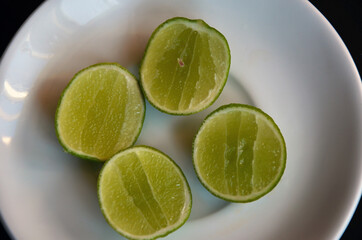 Fresh sliced pieces of lemons on a white plate. High angle of lime fruits slices in a bowl on wooden textured table.
