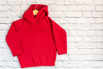 Red kids sweatshirt with hood with clothes hanger on white well brick background. Fashionable...