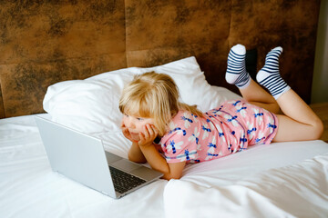 Preschool girl watching videos on laptop, notebook,in bed on clean white linens. Indoors activity...