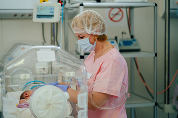 At the intensive care unit. Nurse standing near hospital bed with a baby preparing it for treatment. Newborn is placed in the incubator. Neonatal intensive care unit - obrazy, fototapety, plakaty