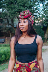 Beautiful African black woman walking in park. Pretty young woman with brown skin. Strong black woman with wearing African print turban and skirt in a tribal pattern.