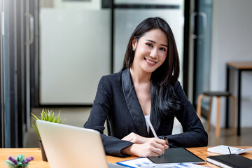 Beautiful young Asian businesswoman holding a pen with a tablet accounting work. Looking at the camera.