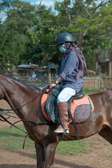 Women with mask and hijab learns to ride a horse. girls riding horses at the ranch. equestrian sport during the pandemic