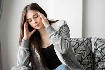 beautiful young brunette woman touching her head suffering from headache or migraine sitting oh sofa at home.