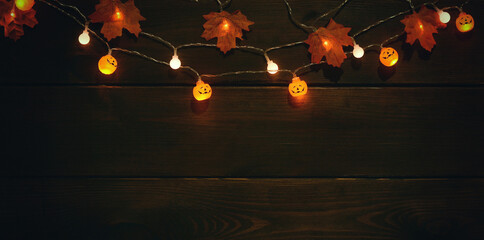 Glowing garlands with halloween pumpkin lamps,leaves on dark wooden background.Banner. Copy space for text