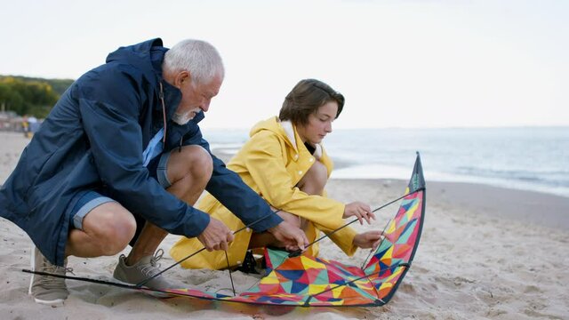 Grandfather with granddaughter on walk on beach at morning, preparing a kite.