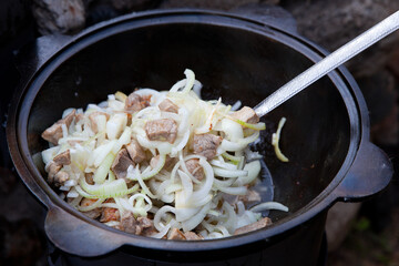 The process of cooking fresh Asian pilaf in a cauldron.The beginning of cooking pilaf, meat and onions