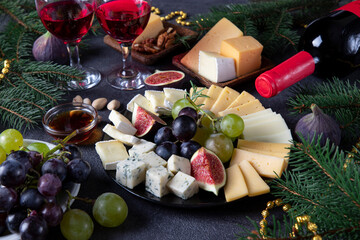 Variety of cheese and fruits served in round plate, on dark gray background with glasses of wine....