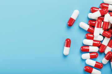 A handful of Red and white pill capsules on a blue background. Free space Top view