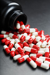 Red and white pills from a black jar on a black background.