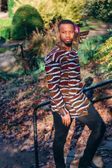 Stylish young African man walking in the park. Handsome young man with brown skin. Stylish black man with afro hair wearing a fashionable African print shirt
