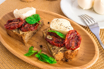 Bruschetta with sun-dried tomatoes, mozzarella and basil, served on a wooden plate.
