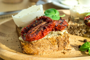 Bruschetta with sun-dried tomatoes, mozzarella and basil, served on a wooden plate.
