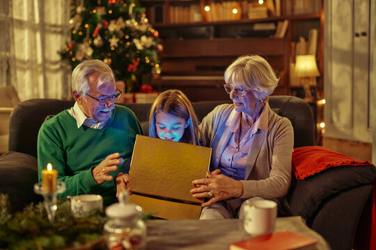 Grandparents and little boy opening Christmas gift at home
