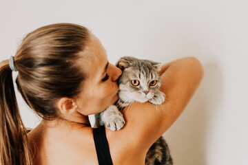 Attractive young woman with long hair embracing her pet with smile. Indoor portrait of cute woman playing with cat. Breed british fold. Healthy lifestyle, harmony and pet.