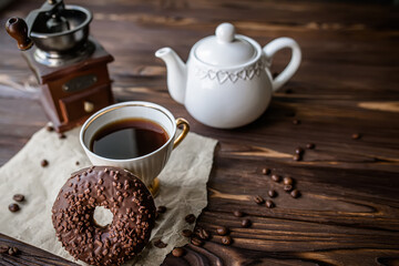 Teapot and cup with freshly brewed coffee on a wooden table. Coffee grinder with coffee beans next to a sweet donut donat.
