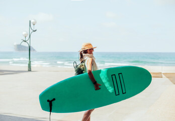 a middle-aged woman holds a green surfboard while walking along the coast on a sunny beach day....