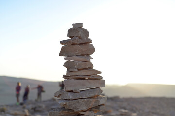 Fototapeta na wymiar Cairn at sunrise, stones balances, pyramid of stones at sunset, concept of life balance, harmony and meditation. A pile of stones in desert mountains, crater Ramon, Israel