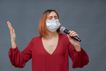 Young beautiful woman in a medical mask stands on a gray background with a phonograph in her hands