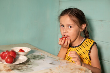 A little girl eats tomatoes in the kitchen sitting at the table