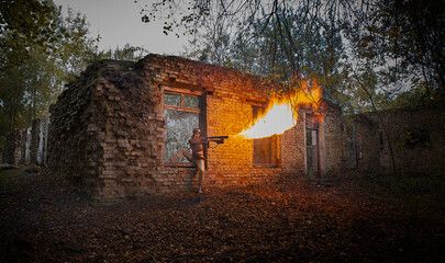 A girl in a military uniform with a flamethrower against the background of an old brick building. - obrazy, fototapety, plakaty
