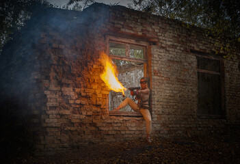 A girl in a military uniform with a flamethrower against the background of an old brick building. - obrazy, fototapety, plakaty