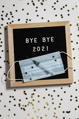 black letter board with text BYE BYE 2021 with small stars, syringe and mask on white background.