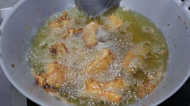 A close-up view of chicken being deep-fried in an iron pan.