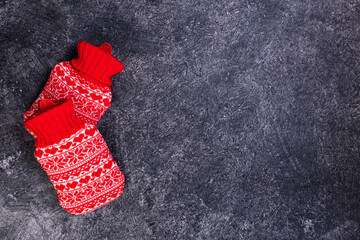 Red knitted hot water bottle with fall autumn leaves and pumpkin on a grey background