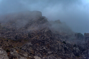 Stony slopes of mountain in dense fog.