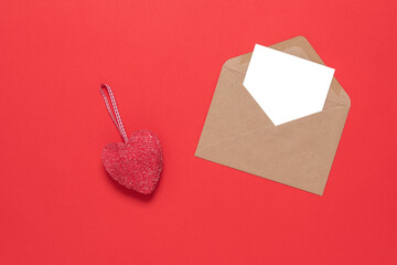 Red heart and blank card mockup in an envelope on a red paper background. Valentine's Day. Top view, flat lay. Textured object.