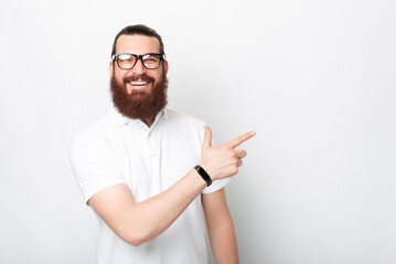 Smiling bearded man is pointing aside on the white background.