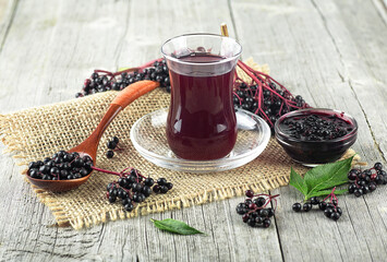 Elderberry syrup in a glass beaker with bunches of elderberries and elderberry leaves on wooden...