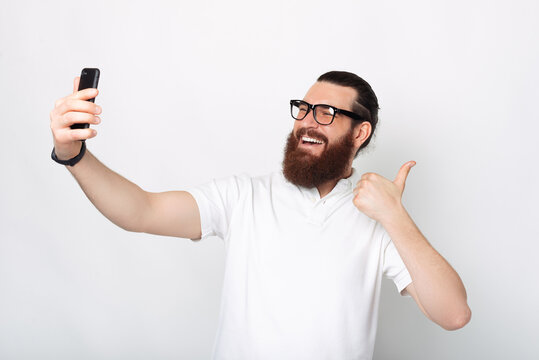 Bearded man is taking a photo of himself with thumb up.