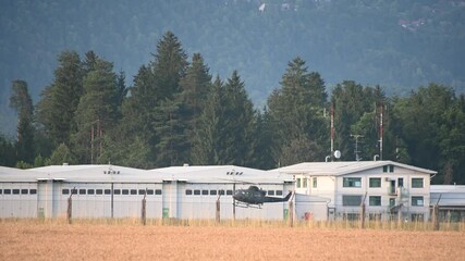Army helicopter landing at Ljubljana Airport, Slovenia. Military chopper hovering. Hangars in the background, security fence in the foreground. Helicopter touchdown. Static shot, real time
