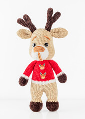 Christmas deer. Soft knitted toy deer in a red jacket on a light gray background, front view, close-up.