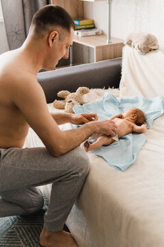 Young dad changing diaper for his newborn son. Lifestyle photo of father caring for his baby. Selective focus. Film grain