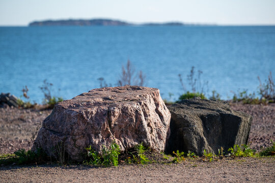 Two blocks of granite casting shadows on the shore with the blue sea in the horizon.